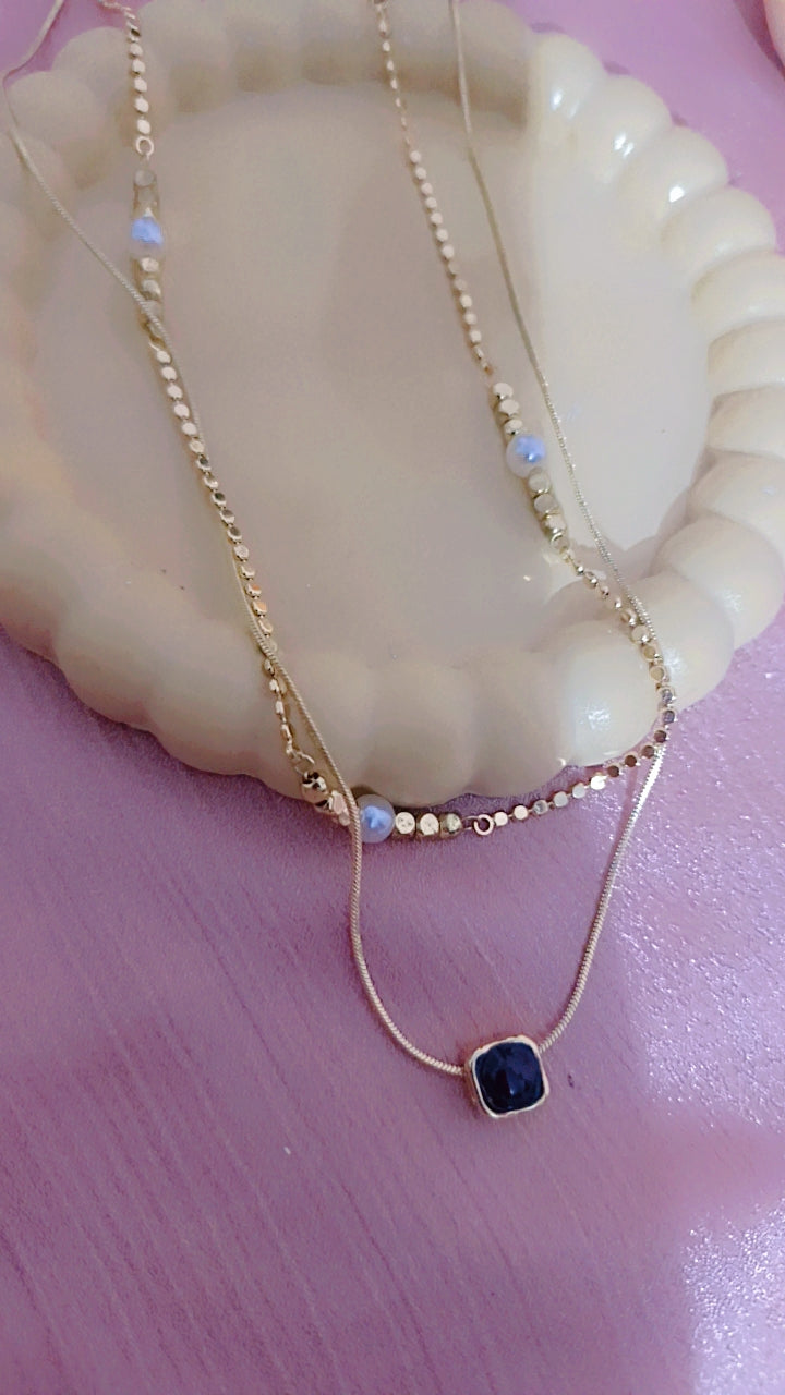 Double Layered Gold Necklace with a Dark Square Pendant and Opal-Look Accents.