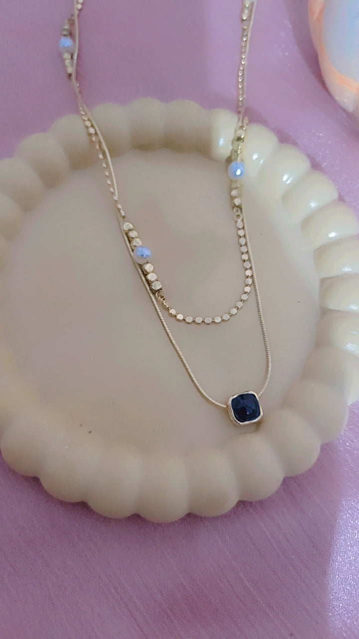 Double Layered Gold Necklace with a Dark Square Pendant and Opal-Look Accents.